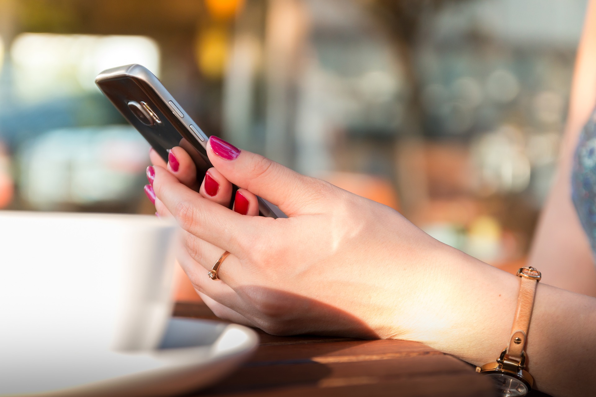Close up of a smartphone being held by a woman at a table in a cafe