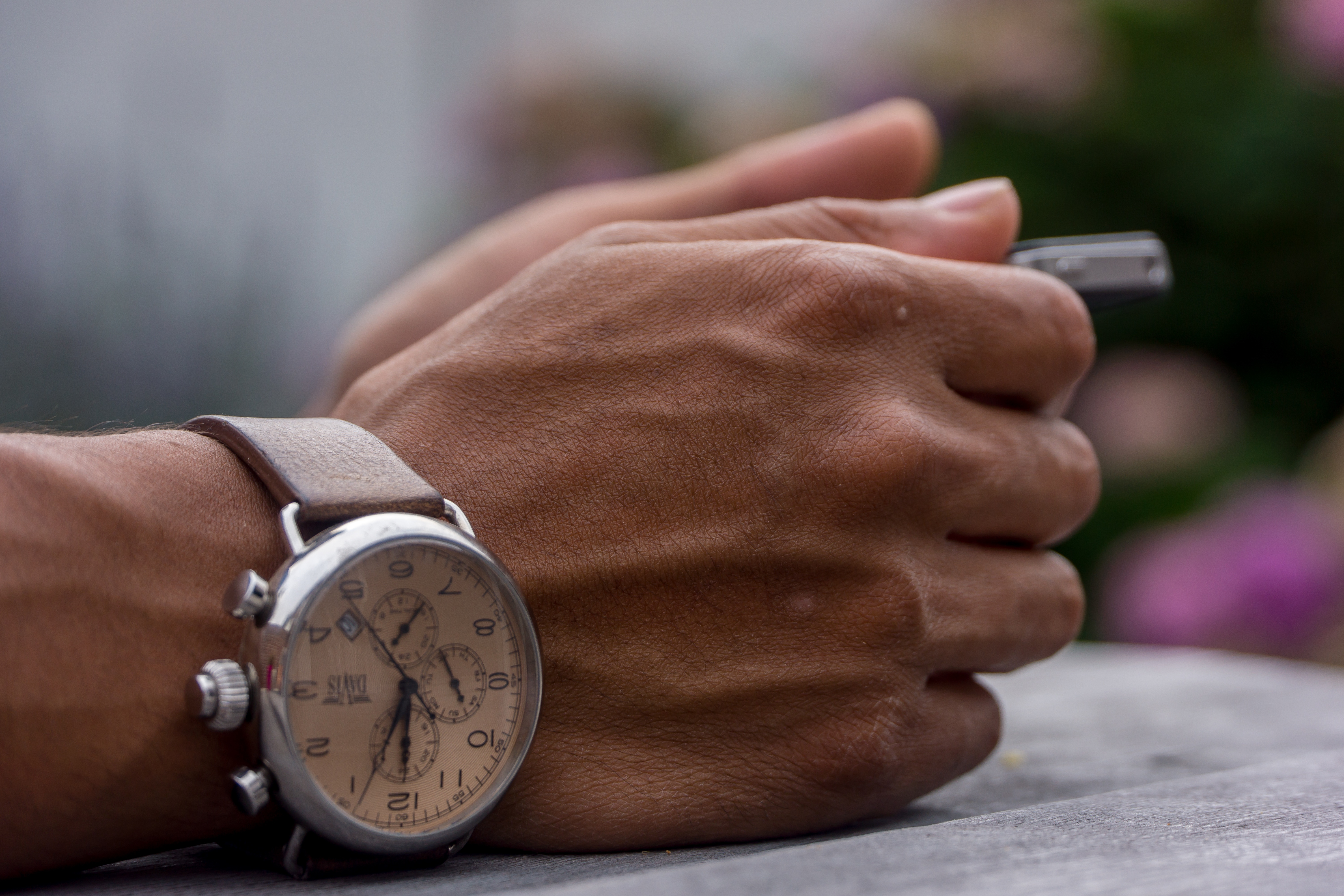 someones hands restingon a table holding a pen with a silver watch with brown leather strap on his wrist